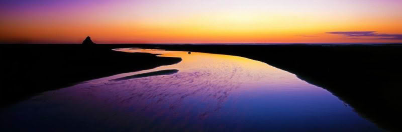 Karekare Beach, New Zealand after sunset as the sun has set and there is a beautiful orange hue throughout the sky