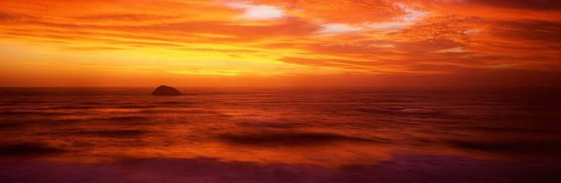 Oaia Island Murawai at sunset with strong orange dusk colours in the sky