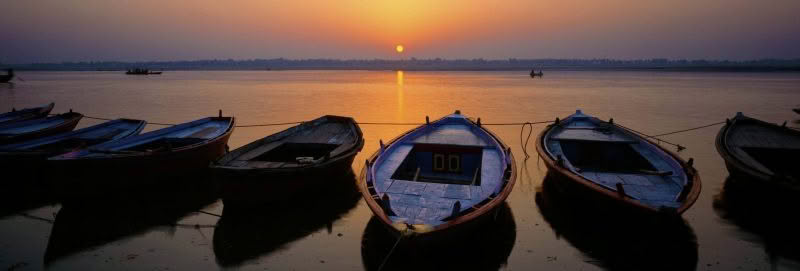 River Ganges Dawn, Varanasi, India. The sun rises over the River Ganges with a row of boats in the foreground