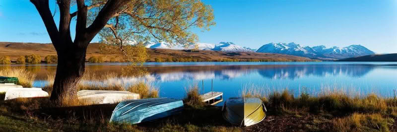 Tranquil, Lake Alexandrina, New Zealand. Row boats and a jetty at the shore of a stunning lake with mountains reflected in the background