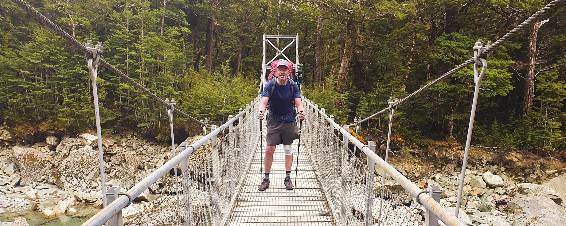 Richard Hume, New Zealand landscape photographer, crossing a swing bridge on the Routeburn Track, New Zealand, while carrying a hiking pack.
