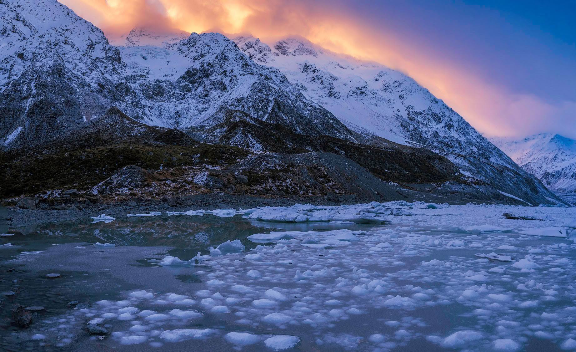 Icebergs at Hooker Lake beneath snow-covered mountains at dusk