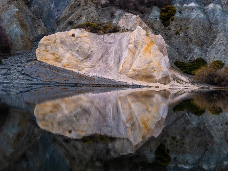Rock formations reflected in the calm waters of Blue Lake at St Bathans in the Maniototo, Central Otago.