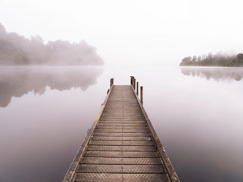 Wooden jetty extending into mist over Lake Mapourika on the West Coast of New Zealand