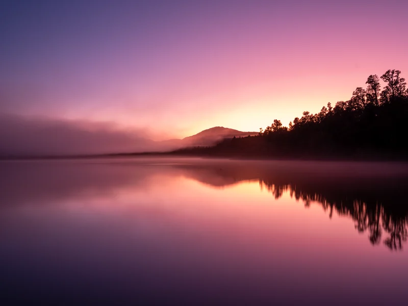 Lake Paringa with pink and purple light reflected through mist on the West Coast of New Zealand